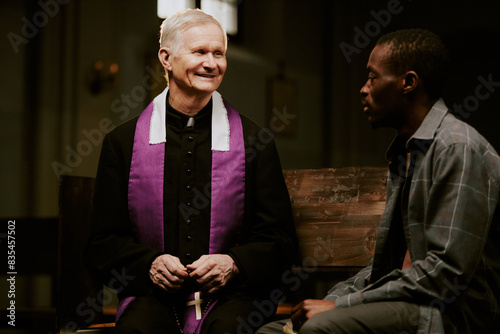 Medium shot of cheerful senior Caucasian Catholic priest talking to African American male churchgoer