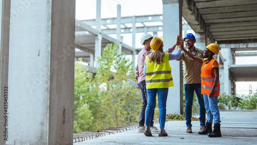 Wallpaper Mural A group of smiling construction workers engage in a high five on a building site, showcasing teamwork in protective gear and casual workwear, with unfinished structures around them. Torontodigital.ca