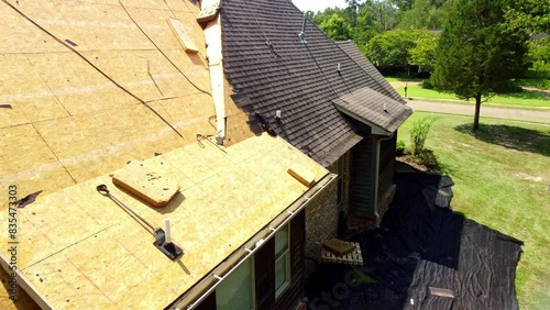 House with new roof being installed, with shingles and exposed deck boards.
