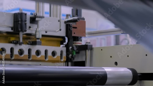 Plastic bag making machine: perforating press unit - production of packaging black bin bags at exhibition,trade show, factory: close up. Concept of recycling, technology equipment, and manufacturing