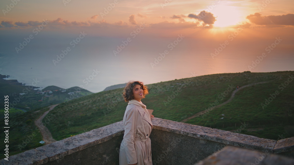 Naklejka premium Smiling woman enjoy sunset overlooking scenic horizon. Stylish traveler relaxing