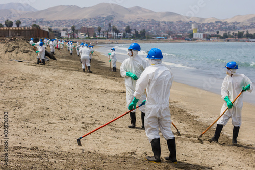 Team of white-clad men cleans oil spill on beach, highlighting environmental disaster response
