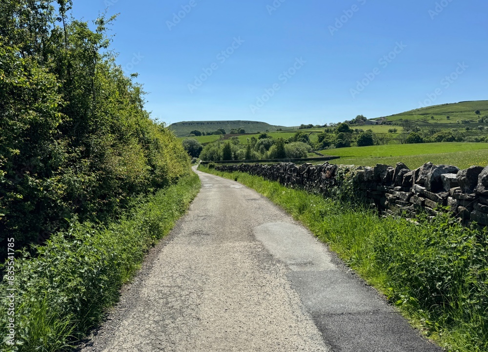 A Lancashire country road winds through a rural landscape beneath a blue sky, with dry stone walls flanking the roadway near Helmshaw, Rossendale, UK. A Lancashire country road winds through a rural landscape beneath a blue sky, with dry stone walls flanking the roadway near Helmshaw, Rossendale, UK.