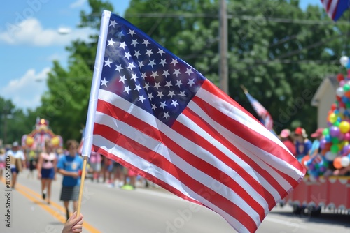 Close-up of the American flag waving in the foreground with a vibrant summer parade taking place in the background during 4 July, independence day of USA