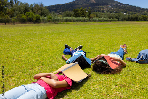 Three children are lying on the grass with books beside them, facing away from the camera