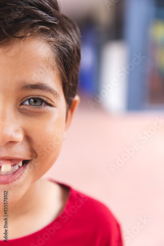 In school, outdoors, a biracial young boy wearing a red shirt is smiling