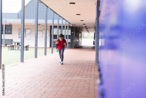 In school, young biracial boy is running along a corridor outdoors