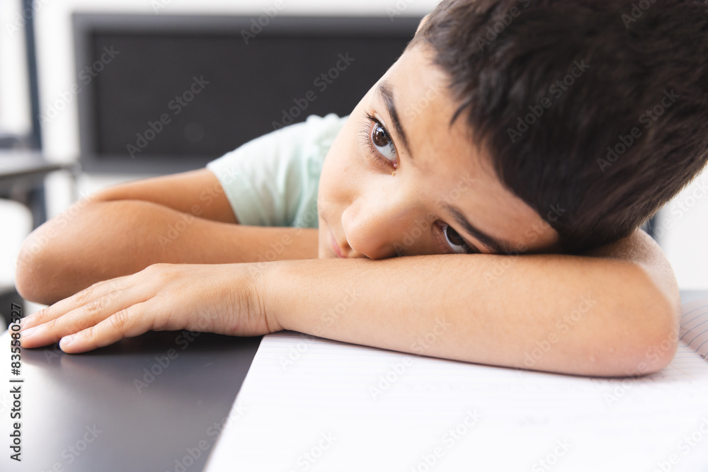 In school, in classroom, biracial young boy leaning on a desk, looking bored