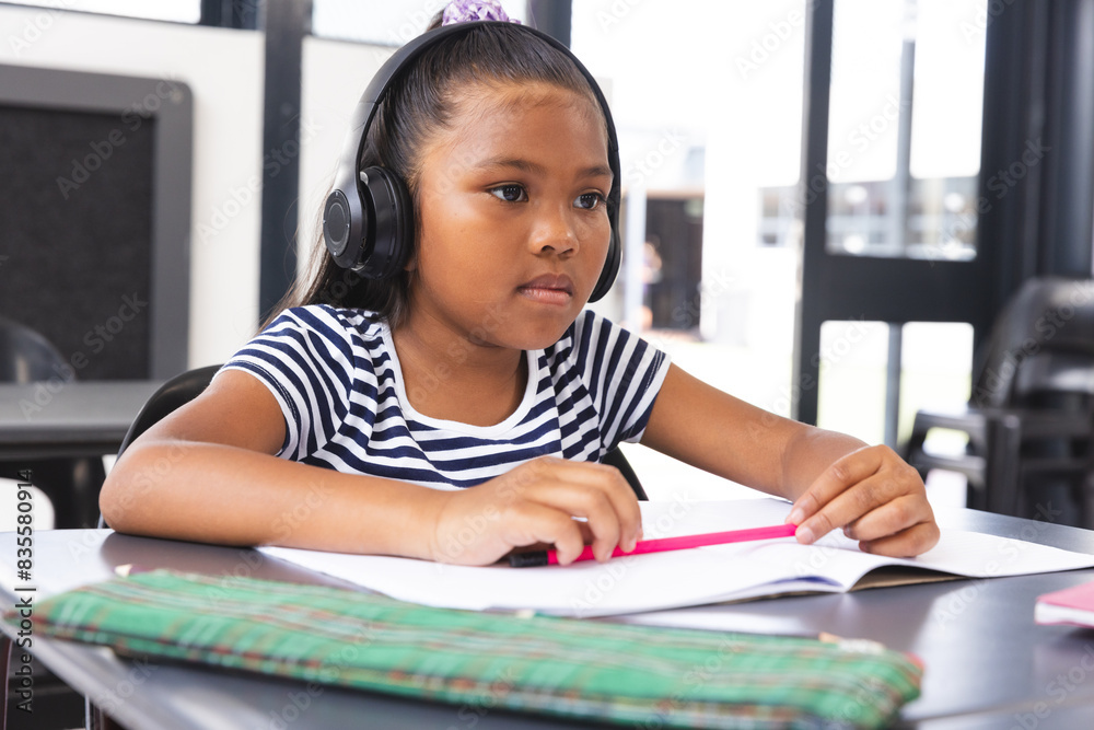 In school, young biracial girl wearing headphones focusing on reading in the classroom In school, young biracial girl wearing headphones focusing on reading in the classroom