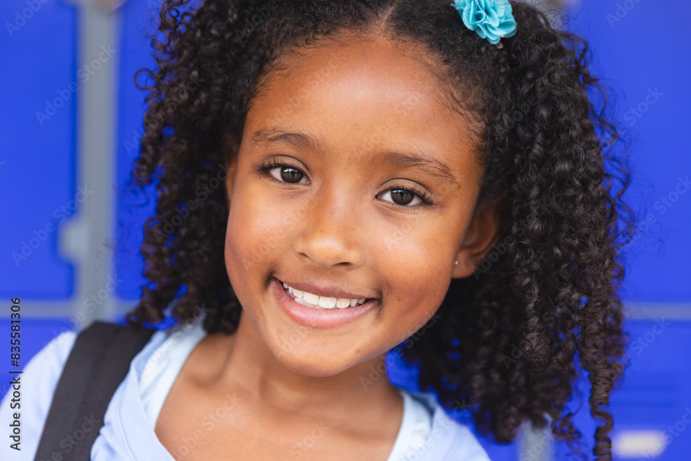 Fototapeta premium Biracial girl smiles brightly in front of a blue door at school