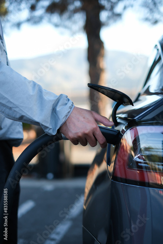 Hand charging EV plug to electric vehicle with natural background for traveling by electric car concept.