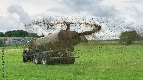 A farm tractor sprays its manure from the tanker onto a field. Manure is used as fertilizer in agriculture.