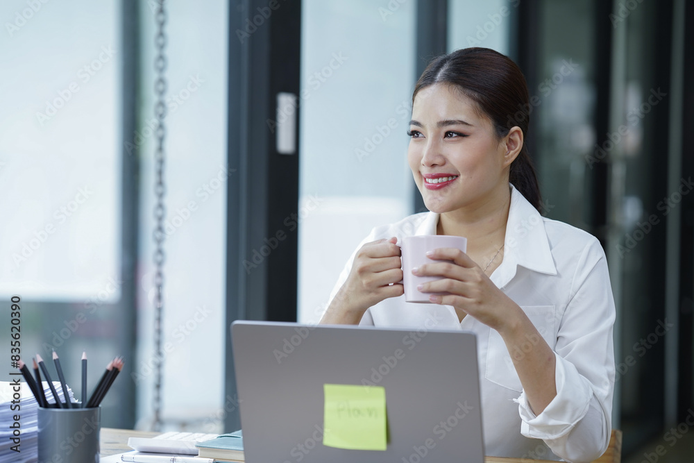 Sharing good business news. Attractive young businesswoman talking on the mobile phone and smiling while sitting at her working place in office and looking at laptop PC. Sharing good business news. Attractive young businesswoman talking on the mobile phone and smiling while sitting at her working place in office and looking at laptop PC.