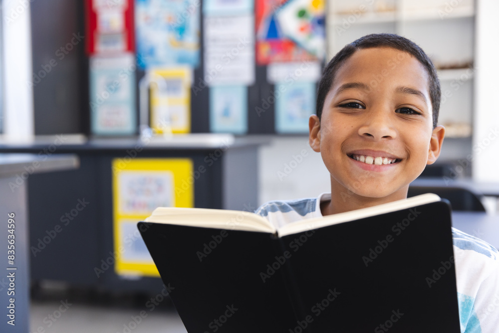 Biracial boy enjoys reading a book in the classroom at school Stock ...