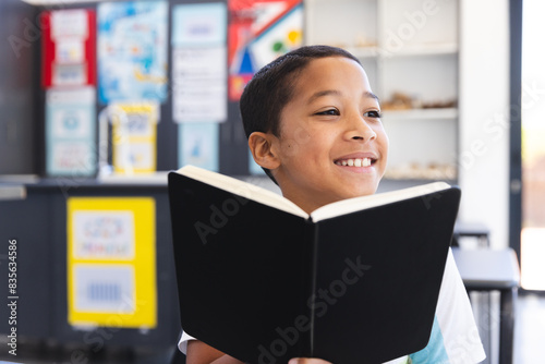 Biracial boy enjoys reading a book in the classroom at school