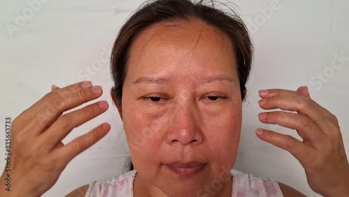
A woman uses her fingers to wipe away wrinkles on her face under the eyes.
