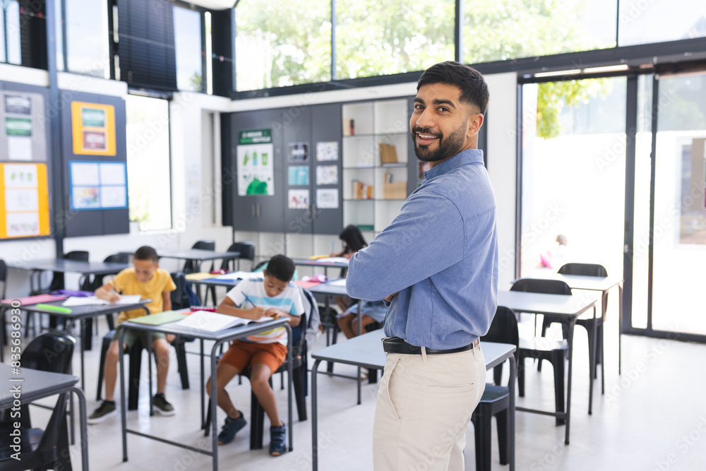 In school, Asian male teacher stands smiling in the classroom, students focusing on work In school, Asian male teacher stands smiling in the classroom, students focusing on work