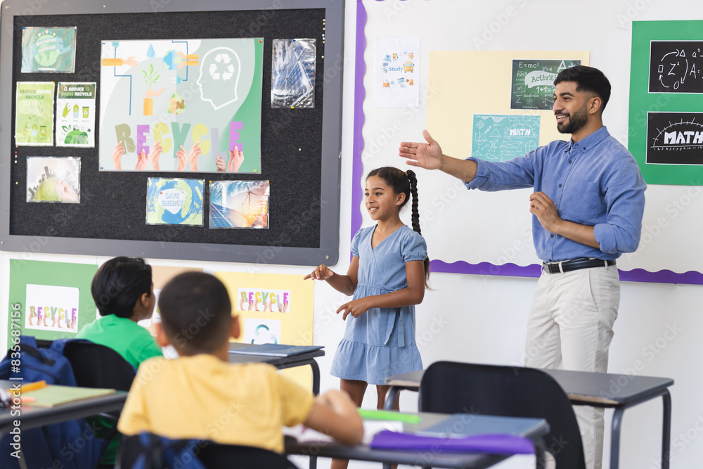 © Wavebreak Media - Young Asian male teacher teaching, biracial girl presenting in a school classroom