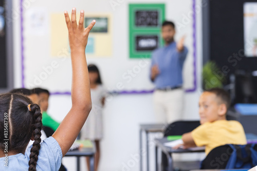 In school, young Asian male teacher stands by a board in the classroom, students raising hands photo