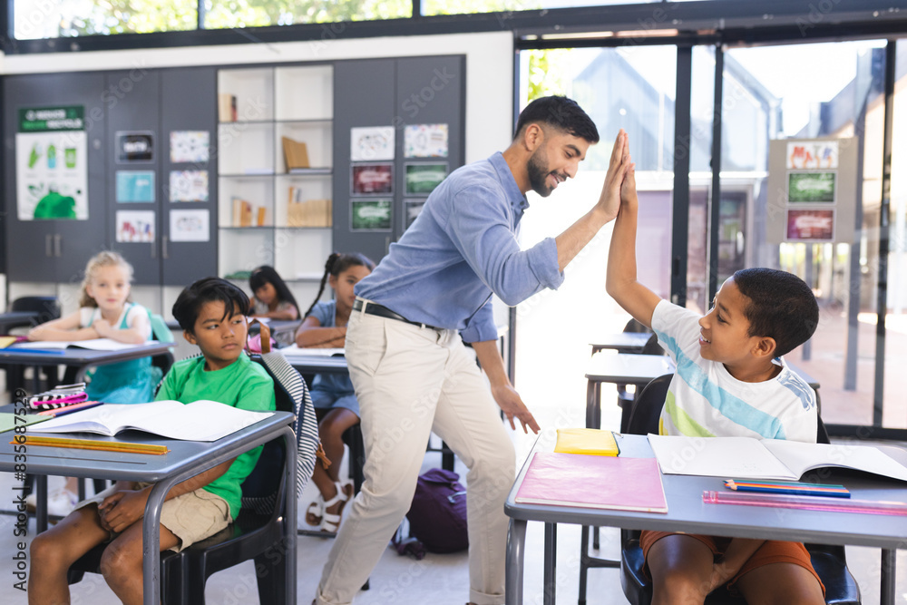 Teacher congratulates a biracial boy with a high-five in a school classroom Teacher congratulates a biracial boy with a high-five in a school classroom