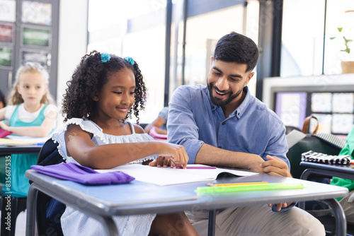 Young Asian male teacher teaching a biracial girl in a school classroom setting