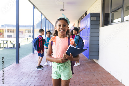 Biracial girl with a blue headband smiles, holding a book at school photo