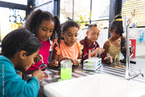 In school, five biracial children are examining science experiments together photo