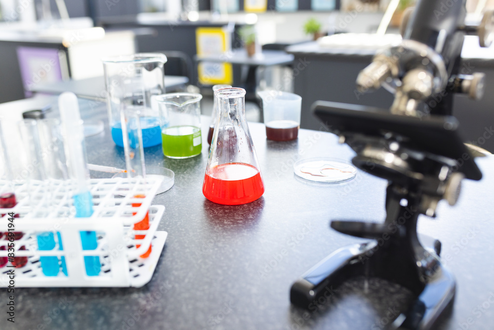 A microscope sits next to colorful liquid-filled beakers and test tubes on a lab bench in school A microscope sits next to colorful liquid-filled beakers and test tubes on a lab bench in school