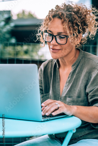 One modern happy serene woman using computer outdoor at home in garden. Pretty female writing on laptop outside house. Alternative workplace and wireless connection technology. People with notebook photo