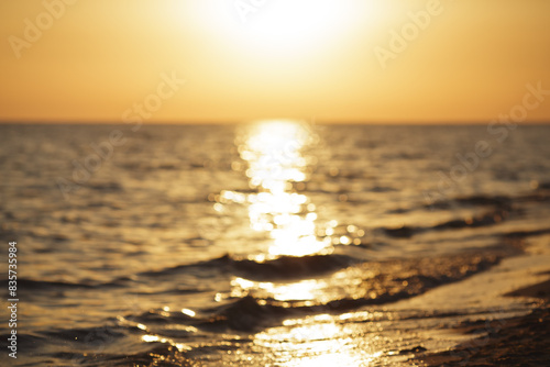 Fototapeta Naklejka Na Ścianę i Meble -  Defocused background, sunset over the ocean with the sun reflecting on the water, creating a golden pathway, waves gently lapping the shore on a peaceful evening