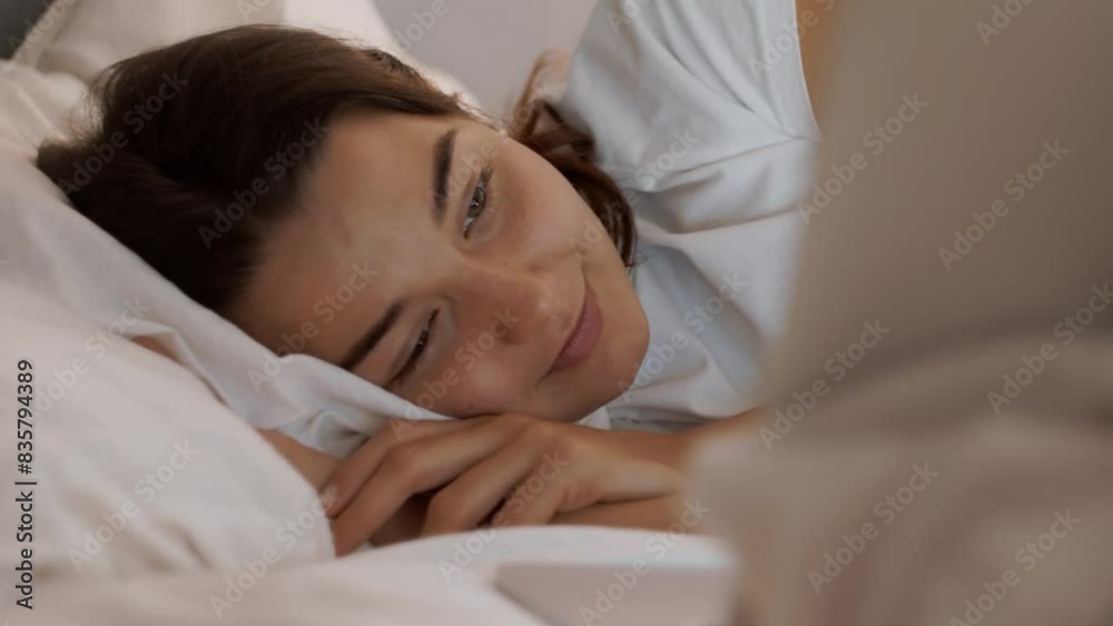 Young woman comfortably lying in bed, using a laptop at evening with soft, warm lighting creating a cozy atmosphere. Cinematic slow motion 4k footage, design for advertising, and social media, vlog Young woman comfortably lying in bed, using a laptop at evening with soft, warm lighting creating a cozy atmosphere. Cinematic slow motion 4k footage, design for advertising, and social media, vlog