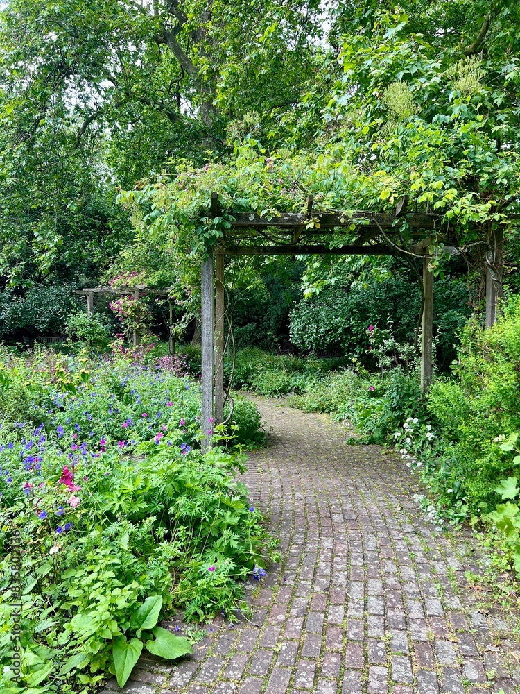 An English Garden with a pergola and lush spring flowers, grass and a cobblestone pathway. Taken during the day, no people. An English Garden with a pergola and lush spring flowers, grass and a cobblestone pathway. Taken during the day, no people.