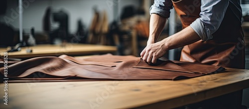 Craftsman with a warm smile, wearing an apron, holds tanned leather rolls in a leather craft workshop, creating a visually appealing copy space image. photo