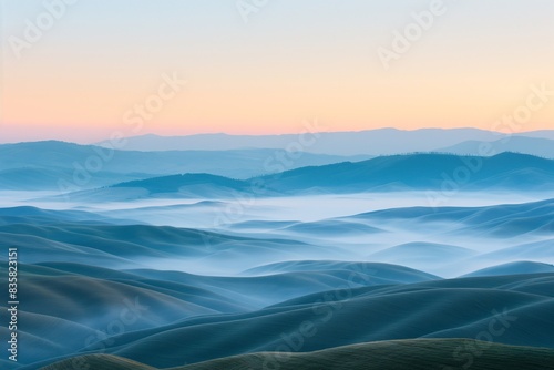 A panoramic view of rolling hills covered in mist during the early morning  the landscape soft and undulating under a gradient sky from dawn s first light.