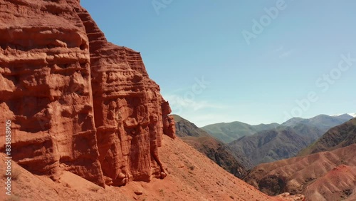 Flying a drone past red dry sandy rocky formations prone to erosion. A journey through the amazing canyons of Konorchek. Trekking in the mountains of Kyrgyzstan. Beautiful mountain summer landscape. photo