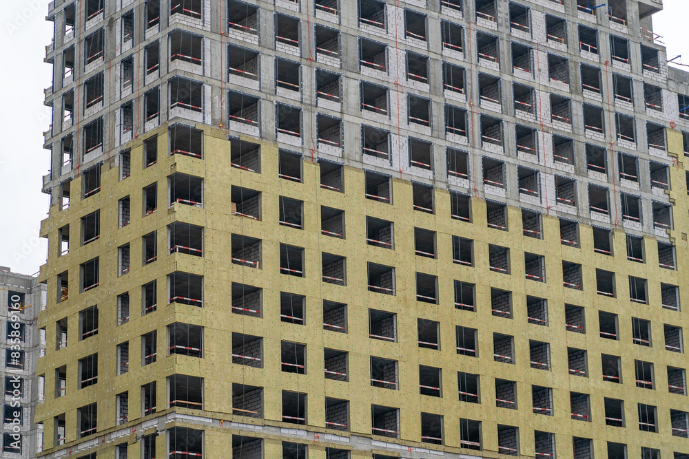 Close-up view of a modern apartment building under construction. The building is partially covered in yellow insulation Close-up view of a modern apartment building under construction. The building is partially covered in yellow insulation
