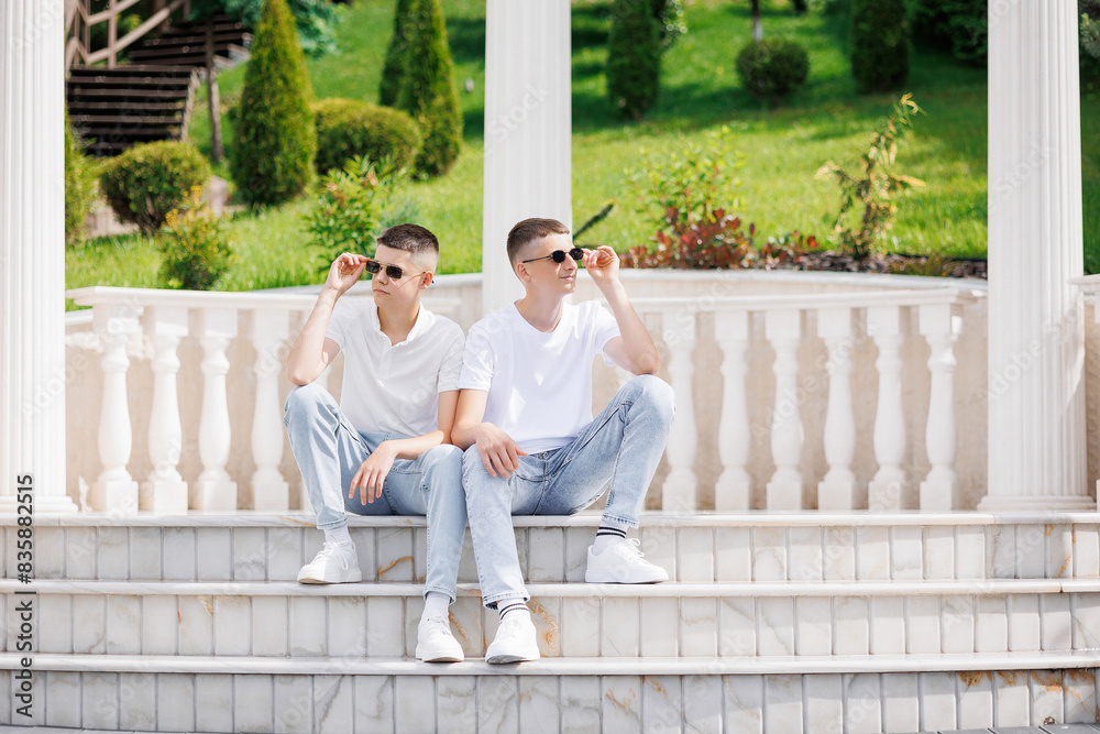 Two men sitting on a white marble staircase, one wearing sunglasses. Scene is relaxed and casual Two men sitting on a white marble staircase, one wearing sunglasses. Scene is relaxed and casual
