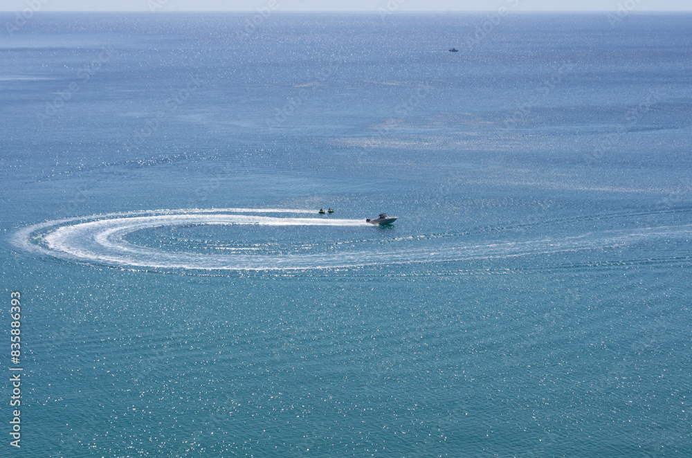 Naklejka premium The turn of the yacht in the form of a loop and tourists engaged in water tubing it happens at a great distance (Rhodes, Greece)