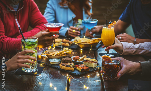 Group of people drinking alcohol and eating appetizers sitting at cocktail bar - Friends enjoying happy hour at brewery pub restaurant - Food and beverage life style concept