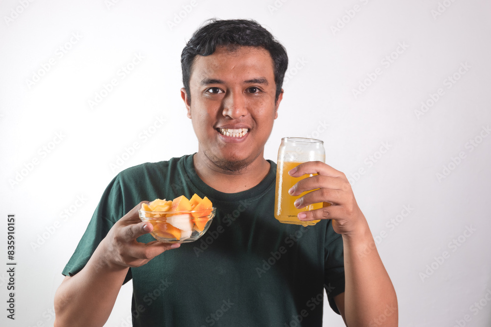 Enjoy healthy food. Handsome young asian man eating fruit salad and orange juice, smiling while standing on white background Enjoy healthy food. Handsome young asian man eating fruit salad and orange juice, smiling while standing on white background