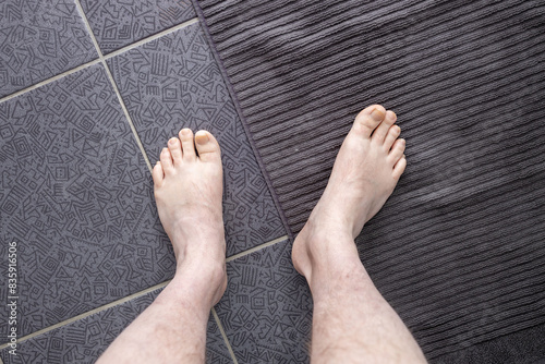 Men's feet on a bath towel in the bathroom on a dark floor