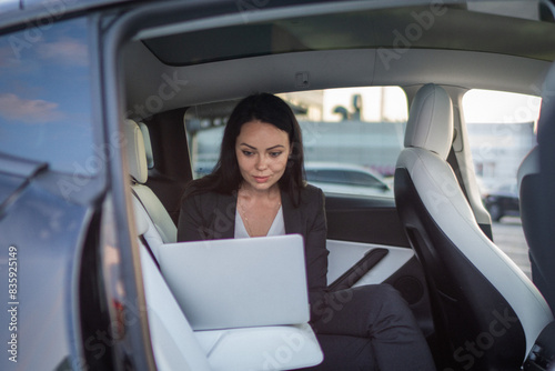 Beautiful businesswoman using laptop while sitting on back seat in the car while working online. Business  people  distance work concept