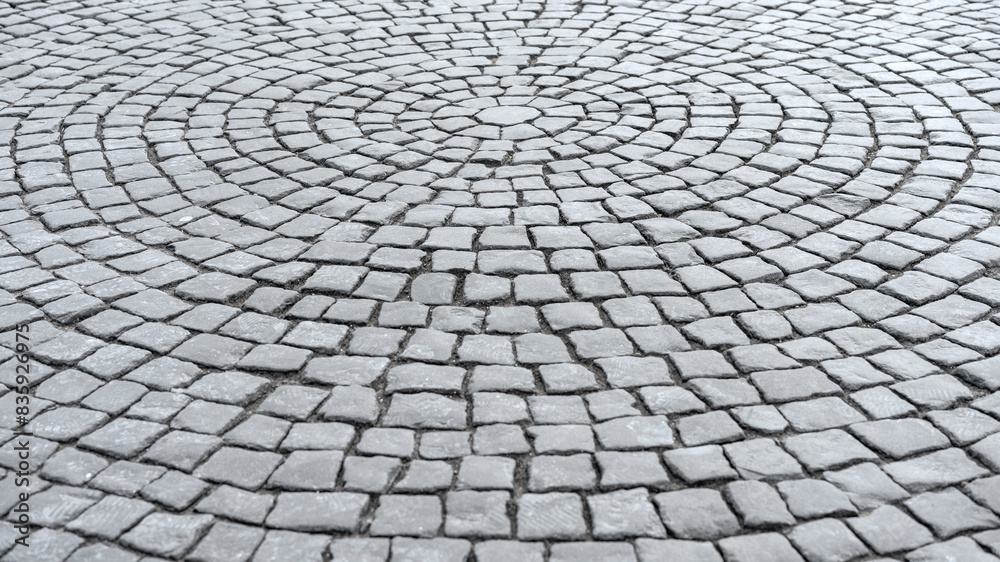 Gray cobblestone pavement arranged in intricate circular pattern. Detailed texture of stone surface highlights geometric design and traditional craftsmanship Gray cobblestone pavement arranged in intricate circular pattern. Detailed texture of stone surface highlights geometric design and traditional craftsmanship