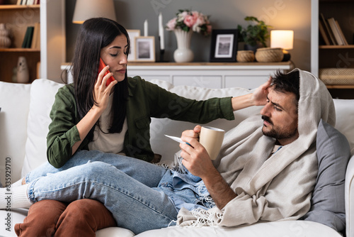 Fotografija Young woman helping and treats her sick man at home who is wrapped in a blanket with a high body temperature
