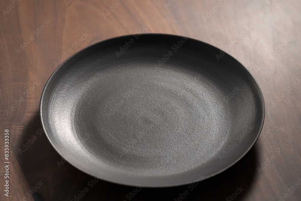 Empty black ceramic hand made plate on walnut wood table Empty black ceramic hand made plate on walnut wood table