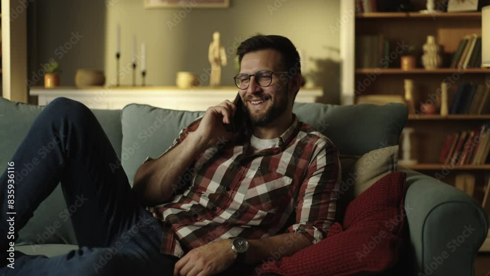 Smiling positive man talking on the phone at home in the evening in the living room, after a working day. Slow-motion shot Smiling positive man talking on the phone at home in the evening in the living room, after a working day. Slow-motion shot
