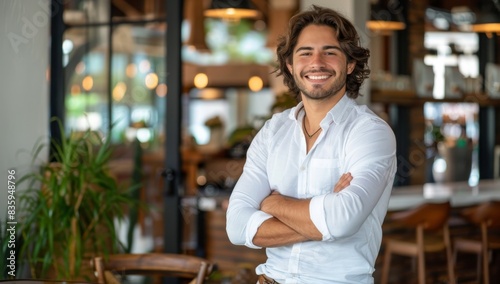 Fototapeta Naklejka Na Ścianę i Meble -  A handsome smiling businessman standing with his arms crossed in an office or coffee shop, or restaurant, exuding confidence and Confident Male Entrepreneur in Coffee Shop With Employee