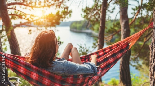 woman relaxing in a red and black hammock by a lake, surrounded by trees during sunset