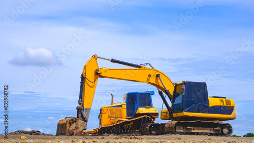 Excavator and dirt grader are leveling the ground for industrial factory construction site area against blue sky background