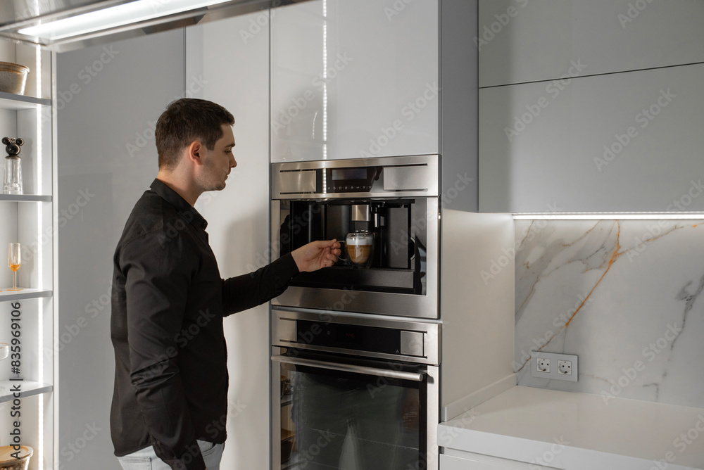A man in a shirt prepares a latte in a built-in coffee maker A man in a shirt prepares a latte in a built-in coffee maker